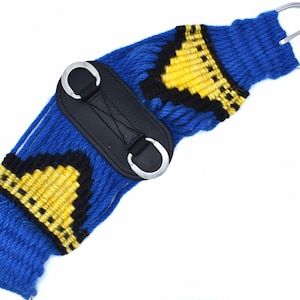 K&ouml;nnte beinhalten: Ein blauer, gewebter Pferdegurt mit schwarzen und gelben geometrischen Mustern. Der Gurt hat ein schwarzes Mittelst&uuml;ck aus Leder mit zwei silbernen D-Ringen und silbernen Beschl&auml;gen. F&uuml;r den Reitsport.