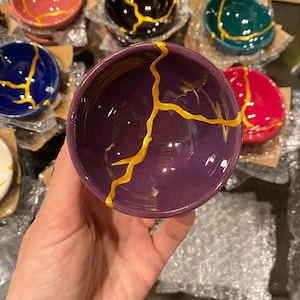 May include: A set of small purple ceramic bowls with gold crackle glaze. The bowls are perfect for serving dips, sauces, or snacks.