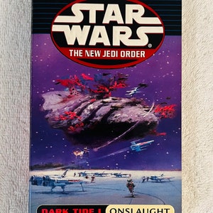 Op de afbeelding: De cover van "Dark Tide I: Onslaught", een Star Wars-roman, toont een ruimtegevecht met X-wing-jagers en een grote, donkere, rotsachtige formatie. Het Star Wars-logo en "The New Jedi Order" zijn ook zichtbaar.