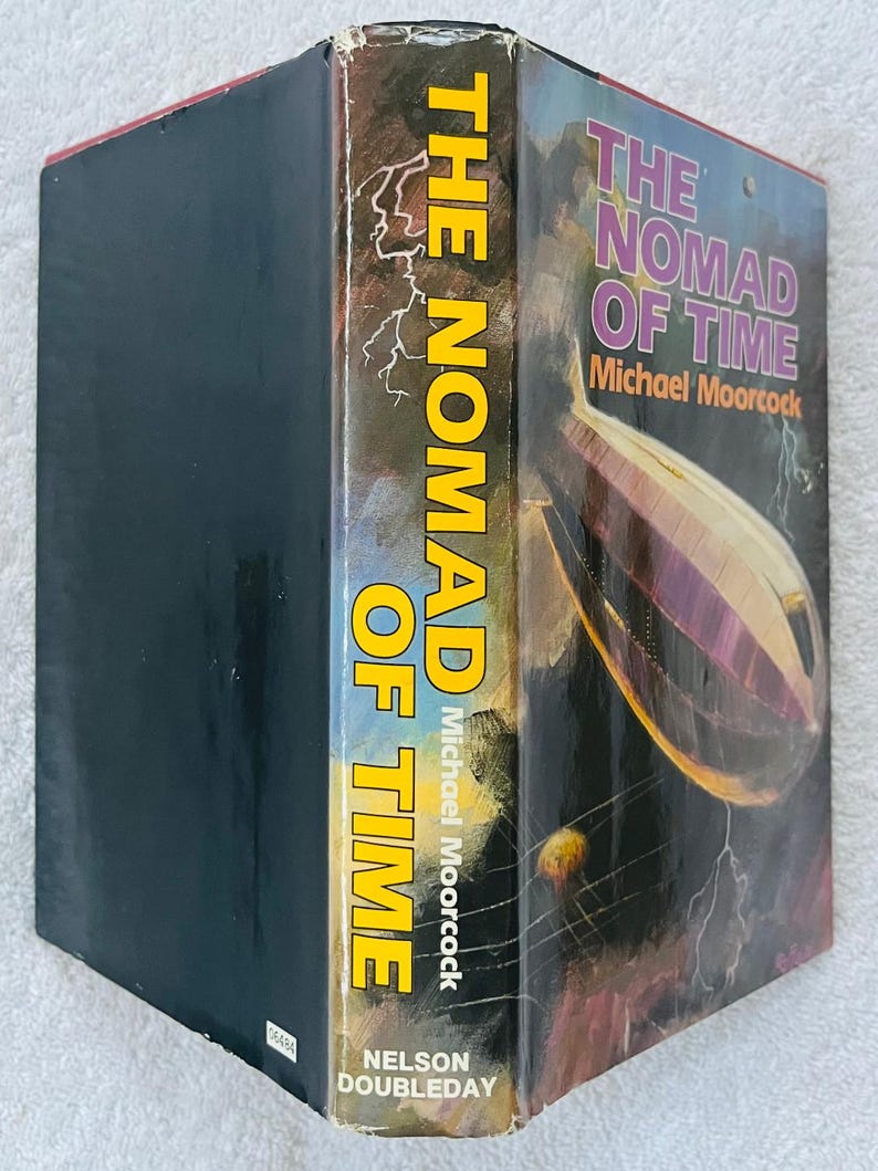 Puede incluir: Un libro de tapa dura titulado "The Nomad of Time" de Michael Moorcock. El lomo es amarillo con el t&iacute;tulo en letras grandes y verticales. La portada presenta una ilustraci&oacute;n de dirigible p&uacute;rpura sobre un fondo oscuro.