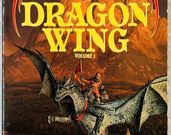 Könnte beinhalten: Ein Taschenbuch mit dem Titel Dragon Wing, Volume 1, aus dem Death Gate Cycle von Margaret Weis und Tracy Hickman. Das Cover zeigt einen grünen Drachen mit einem Reiter, der über eine Landschaft mit einer großen Burg und Bergen fliegt.