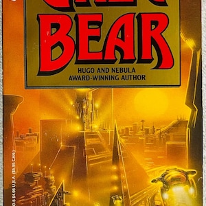 May include: A paperback book titled "Queen of Angels" by Greg Bear. The cover features the author's name in large red letters, a futuristic cityscape, and the quote "Succeeds on Virtually Every Level." from the New York Times Book Review.