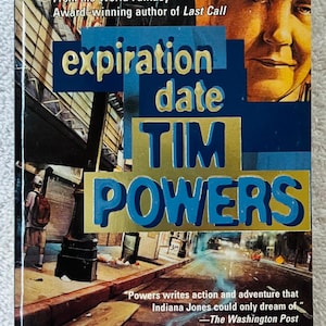 May include: A paperback book titled "Expiration Date" by Tim Powers. The cover features a street scene with the title in blue and gold lettering. The author's name is also in blue and gold. A quote from The Washington Post is included.