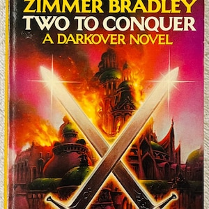 May include: A vintage paperback book titled "Two to Conquer" by Marion Zimmer Bradley. The cover art depicts two crossed swords against a fantasy landscape with a fiery sky. The book is from DAW Books.
