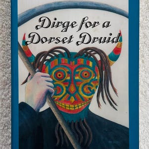 May include: A book cover with a blue border and orange top section. The title "MARGOT ARNOLD" is in black text. The book's title is "Dirge for a Dorset Druid". The cover art features a colorful mask and a figure holding a staff.