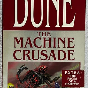 May include: A paperback book titled "Dune: The Machine Crusade" by Brian Herbert and Kevin J. Anderson. The cover features a red and silver design with the text "The New York Times Bestseller." An illustration of a mechanical creature is also visible.