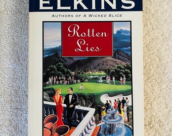 May include: A paperback book titled "Rotten Lies" by Charlotte and Aaron Elkins. The cover shows a golf course scene, a red-boxed title, and a quote from the Houston Chronicle.