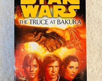 May include: A hardback book titled "Star Wars: The Truce at Bakura" by Kathy Tyers. The cover features Luke Skywalker, Han Solo, and Princess Leia. The background is a fiery orange and red with a gloved hand and rope.