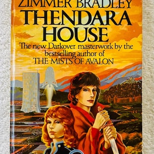 May include: Vintage paperback book cover for "Thendara House" by Marion Zimmer Bradley. The cover shows two women, one with a sword, set against a futuristic city and sunset. The title and author's name are clearly visible.