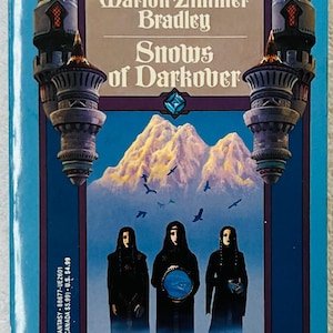 May include: A vintage paperback book titled "Snows of Darkover" by Marion Zimmer Bradley. The cover features a mountain range, three figures, and the text "DARKOVER" and "Edited by". The book has a blue border and a fantasy theme.