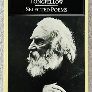 Puede incluir: Una edición de Penguin Classics de "Selected Poems" de Henry Wadsworth Longfellow. La portada del libro presenta un retrato en blanco y negro del autor con el título en texto blanco. El libro tiene un borde amarillo.