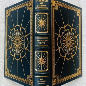 Op de afbeelding: Een donkerblauw gebonden boek getiteld In Search of History door Theodore H. White, uitgegeven door The Franklin Library. De kaft en rug zijn voorzien van gedetailleerde goudfoliebedrukking met geometrische sterpatronen en randen.