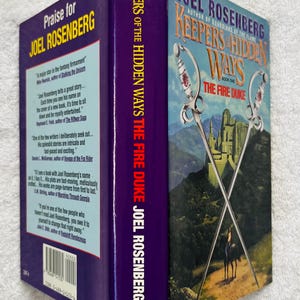 May include: A hardcover book titled "Keepers of the Hidden Ways: The Fire Duke" by Joel Rosenberg. The cover features crossed swords, a castle, and a person on horseback. The spine is purple with the author's name.