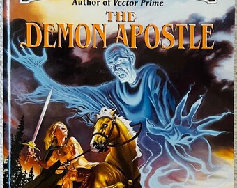 May include: A paperback book titled The Demon Apostle by R.A. Salvatore. The cover art depicts a person on a brown horse holding a sword, facing a large, translucent blue spectral figure. Below, two figures stand near a castle on a rocky shore.