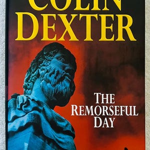 May include: Hardcover book titled "The Remorseful Day" by Colin Dexter. The cover features a blue statue against a red background, with yellow text at the top. A small figure plays a horn.