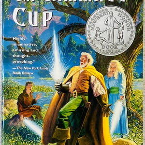 May include: The Gammage Cup by Carol Kendall, a paperback book with a cover illustration featuring three figures in a forest setting. A central figure holds a glowing light, while a Newbery Honor Book seal is printed in the upper right corner.