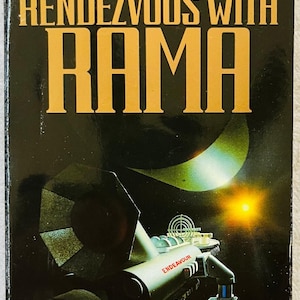 May include: A vintage paperback book titled "Rendezvous With Rama" by Arthur C. Clarke. The cover features a spaceship labeled "Endeavour" against a dark space background with a bright sun and a crescent shape. The book is a Hugo and Nebula Award-winning novel.