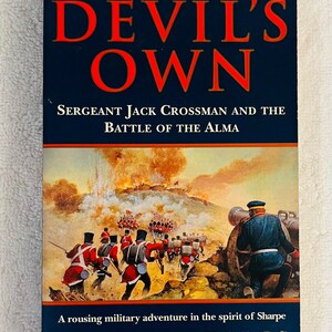 Może przedstawiać: Twarda oprawa książki zatytułowana "THE DEVIL'S OWN" z granatową okładką i pomarańczowymi literami. Ilustracja na okładce przedstawia scenę bitwy wojskowej. Nazwisko autora, Garry Douglas, znajduje się na dole.