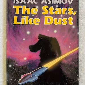 Könnte beinhalten: Ein Vintage-Taschenbuch mit dem Titel "The Stars, Like Dust" von Isaac Asimov. Das Cover zeigt eine Weltraumszene mit einem Raumschiff, einem Lichtstrahl und einer dunklen Silhouette vor einem lila und sternenübersäten Hintergrund. Der Titel ist gelb.