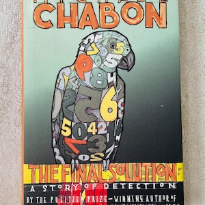 May include: A paperback book titled "THE FINAL SOLUTION" by Michael Chabon. The cover features a parrot illustration composed of numbers against a green and black gradient background. The author's name is in orange letters.