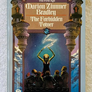May include: A vintage paperback book titled "The Forbidden Tower" by Marion Zimmer Bradley. The cover depicts a woman in a red dress with arms raised, surrounded by figures, against a blue and purple backdrop. The book has a light blue border and two tower illustrations.