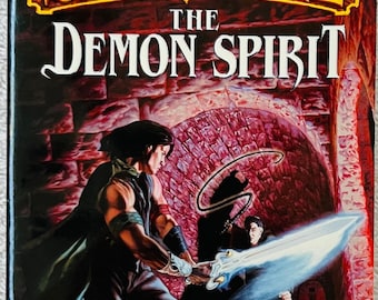 May include: A paperback book titled The Demon Spirit by R.A. Salvatore, author of The Forgotten Realms novels. The cover art depicts a dark-haired figure in a green cloak wielding a glowing blue sword against a shadowy opponent in a red stone dungeon.