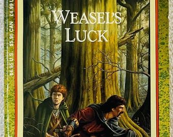 May include: A paperback book titled "Weasel's Luck" from the Dragonlance Heroes series. The cover art depicts two figures with swords in a forest setting. The book has a green and yellow border with the author's name, Michael Williams, at the bottom.