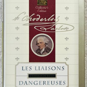 Puede incluir: Un libro de tapa dura titulado "Les Liaisons Dangereuses" de Choderlos de Laclos, una edición de coleccionista de The New York Public Library. La portada presenta un retrato y motivos decorativos de flor de lis.