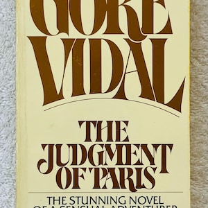 May include: A vintage paperback book titled "Gore Vidal" with the title "The Judgment of Paris" in brown lettering on a cream background. The cover also includes the text "The Stunning Novel of a Sensual Adventurer".