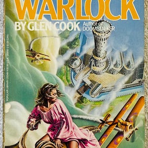 May include: Vintage paperback book cover for "Darkwar Trilogy 2: Warlock" by Glen Cook. The cover art features a woman in a pink dress riding a fantastical vehicle, with biplanes and a castle in the background. The book is from the Questar Science Fantasy series.