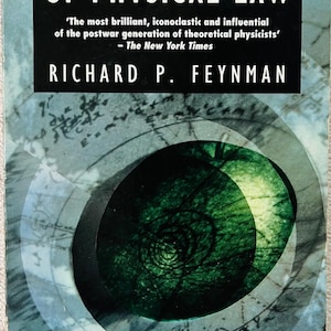 May include: A paperback book titled The Character of Physical Law by Richard P. Feynman. The cover features a black rectangular header with white text, a central dark green circular graphic, and faint mathematical equations in the background.
