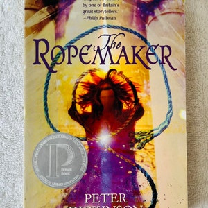 May include: A book cover for "The Ropemaker" by Peter Dickinson. The cover features a stylized image of a person with a rope around their neck. The title is in large, purple letters. A silver seal reads "Honor Book".