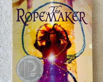Op de afbeelding: Boekomslag van "The Ropemaker" van Peter Dickinson. De afbeelding toont een persoon met een touw om de nek, met de titel in grote, paarse letters. Een zilveren zegel leest "Honor Book". Er staat ook een citaat van Philip Pullman.