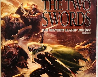 May include: A paperback book titled The Two Swords by R.A. Salvatore, part of The Hunter's Blades Trilogy Book III. The cover features a central figure with long white hair and a green cloak fighting multiple snarling, dark-furred creatures.