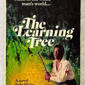Pu&ograve; includere: Copertina di un libro tascabile vintage per "The Learning Tree" di Gordon Parks. La copertina presenta un uomo che tiene un bastone, con il titolo in grandi lettere bianche. Lo sfondo &egrave; un mix di verde e giallo.