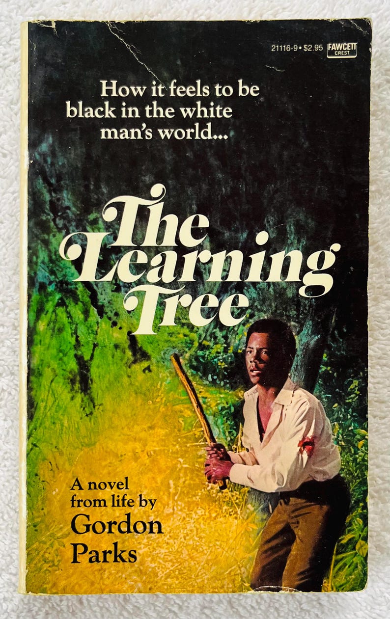 Pu&ograve; includere: Copertina di un libro tascabile vintage per "The Learning Tree" di Gordon Parks. La copertina presenta un uomo che tiene un bastone, con il titolo in grandi lettere bianche. Lo sfondo &egrave; un mix di verde e giallo.