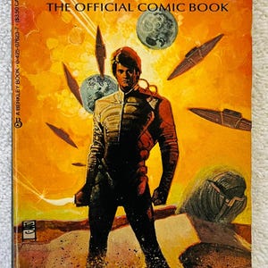 May include: Vintage "Dune: The Official Comic Book" by Marvel Comics. The cover features a figure in a futuristic suit, set against a vibrant orange and yellow background with spacecraft and planets. The book's title is prominently displayed.