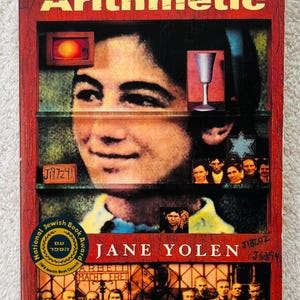 May include: Book cover for "The Devil's Arithmetic" by Jane Yolen. The cover features a portrait of a young person, with a red and brown background. The title is in gold lettering. The book has a National Jewish Book Award sticker.
