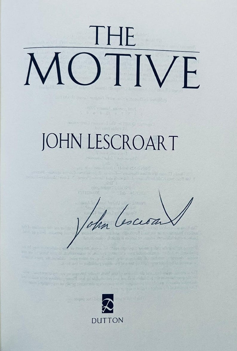 May include: A book cover with the title "THE MOTIVE" in dark blue capital letters. Below the title is the author's name, "JOHN LESCROART", also in dark blue. The author's signature is present, along with the publisher's logo and name, "DUTTON".