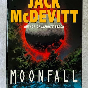 Può includere: Copertina del libro "Moonfall" di Jack McDevitt. Il titolo è in bianco, il nome dell'autore in giallo e lo sfondo presenta una luna scura con un anello rosso, alberi e una casa.
