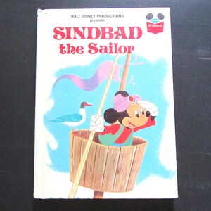 May include: A vintage children's book cover featuring Mickey Mouse dressed as a sailor, holding a rope and looking out at the sea. The book title is "Sindbad the Sailor" and is presented by Walt Disney Productions.