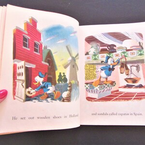 May include: An open book with illustrations of Donald Duck wearing blue sailor clothes. The left page shows Donald Duck in Holland, holding a wooden shoe. The right page shows Donald Duck in Spain, holding a sandal. The text on the left page reads "He set out wooden shoes in Holland". The text on the right page reads "and sandals called zapatas in Spain."