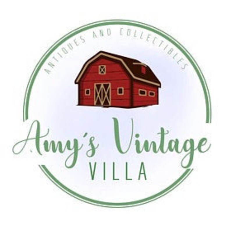 May include: A red barn with white windows and a white roof, surrounded by a blue and green circle with the text "Antiques and Collectibles Amy's Vintage Villa".
