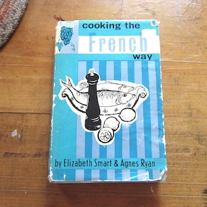 May include: Vintage cookbook titled "Cooking the French Way" with a blue cover and a graphic of fish, a pepper grinder, and lemons. The book is by Elizabeth Smart & Agnes Ryan.