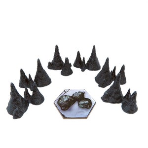 Puede incluir: Un conjunto de 12 piezas de terreno montañoso dentado, impresas en 3D y de color negro, para juegos de mesa. Las piezas están dispuestas en círculo alrededor de una baldosa hexagonal con un diseño gris y blanco.