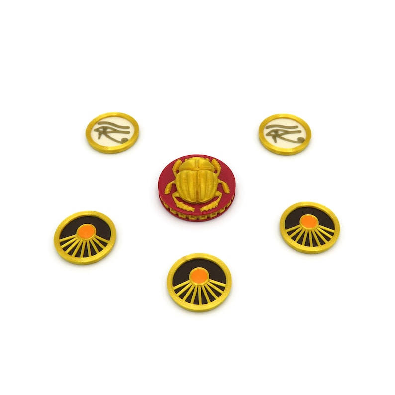 May include: Six gold-colored game pieces with different symbols. One piece features a red background with a gold scarab beetle. Two pieces feature a white background with a gold eye of Horus symbol. Three pieces feature a black background with a gold sun symbol.