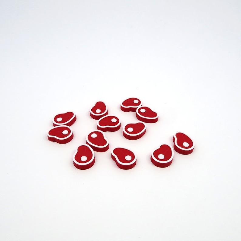 May include: A group of 12 red and white plastic game pieces shaped like a steak.