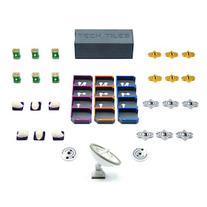 Puede incluir: Un conjunto de piezas de juego, que incluye una caja gris con la inscripción "TECH TILES", bandejas coloridas y varias fichas. Las piezas están dispuestas sobre un fondo blanco, lo que sugiere un juego de mesa o un conjunto educativo.