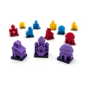 Może przedstawiać: Kolekcja kolorowych miniaturowych modeli budynków w kolorach czerwonym, niebieskim, żółtym i fioletowym. Modele przedstawiają różne style architektoniczne, w tym kopuły i wieże, na białym tle.