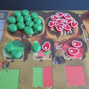 May include: A game board with green and red game pieces. The green pieces are shaped like cabbages and the red pieces are shaped like steaks. There are also two smaller game boards with green and red pieces.